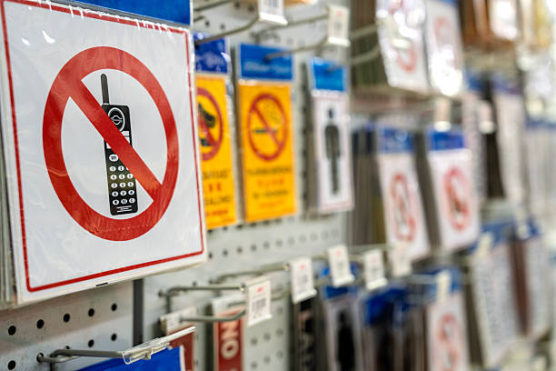 Close-up view of a “no mobile phone” sign with various sign on a product display wall inside a retail store.