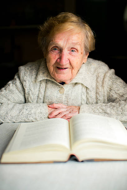 istock An elderly woman sits at a table reading a thick book, immersed in quiet concentration and surrounded by a sense of wisdom and calm. 2213480442