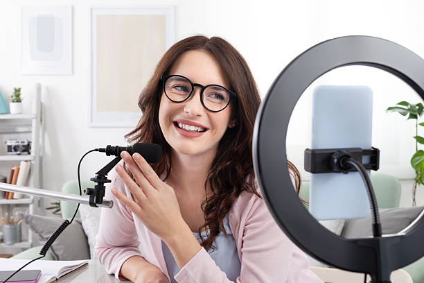 istock Smiling young female content creator and influencer at home, using a smartphone and ring light, speaking into a microphone. Live streaming, podcasting or recording videos and content for social media 2213481820