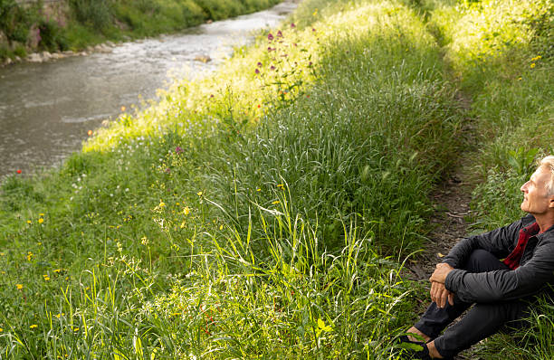 Mature man pauses by water's edge in springtime, Liguria