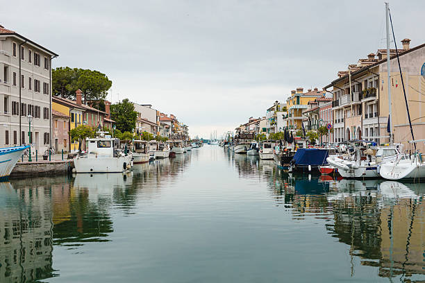 A tranquil view of the canal running through the town of Grado, with boats moored along the banks and colorful buildings. Grado, Friuli Venezia Giulia, Italy.