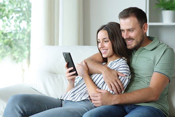 istock Happy couple using mobile phone together at home 2213486159