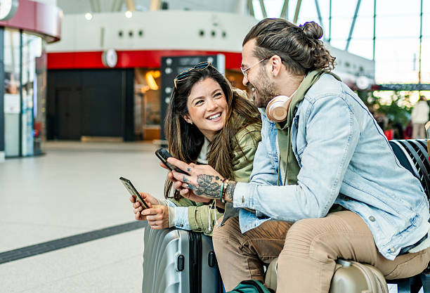 istock Young couple using mobile phones while waiting at the train station 2213488567