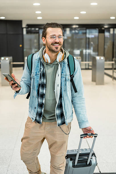 istock Tourist walking through airport terminal holding smartphone and pulling suitcase 2213489792