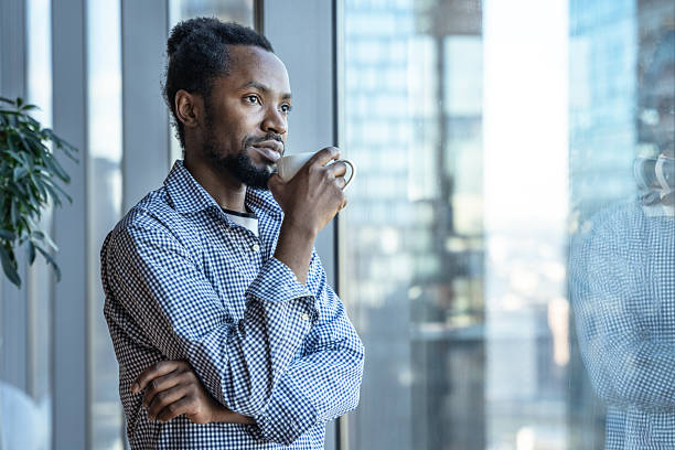 Thoughtful Man Enjoying Coffee Near Window in Bright Modern Office Setting