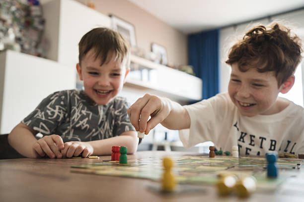 Two cheerful children play a board game in a cozy room, enjoying laughter and fun moments. They focus on the game pieces while sharing a joyful bonding experience, surrounded by a relaxed indoor atmosphere.