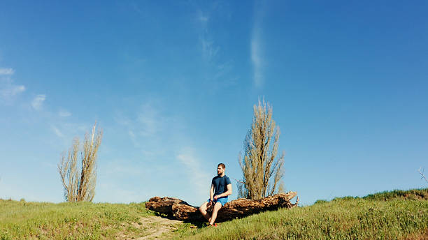 istock Young man resting on a fallen tree trunk enjoying the landscape 2213503974
