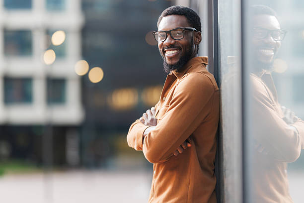 istock Confident man smiling outdoors while leaning against reflective glass in urban setting 2213505372