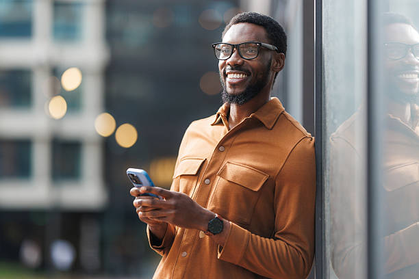 istock Smiling man using smartphone outdoors with modern office buildings in background 2213505407