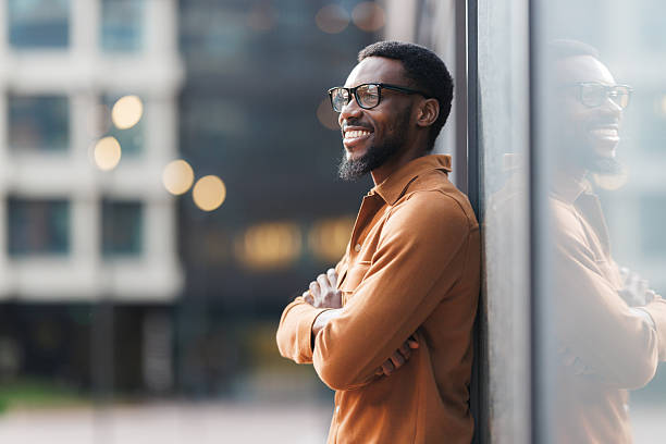 Smiling man standing outdoors with arms crossed, surrounded by modern architecture