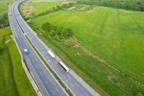 istock Traffic flows along a highway bordered by vibrant green fields and trees near a rural area in daylight hours 2213505904