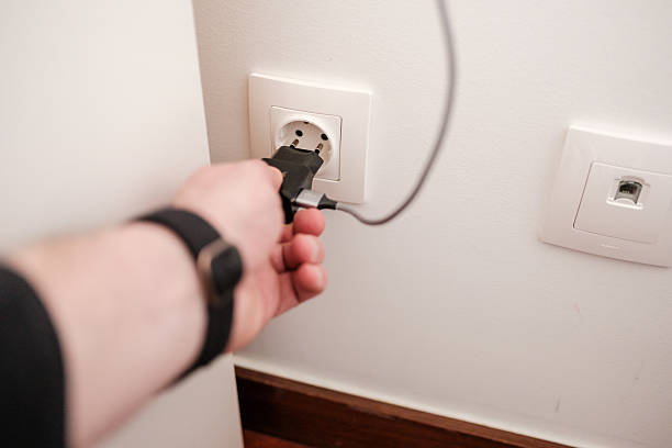istock Person plugging a black charger into a white wall socket 2213509204