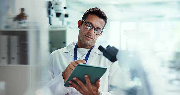 istock Scientist, man and tablet with research in lab for medical study by container, review or vaccine development. Person, touchscreen and chemical analysis with pharmaceutical test on app by microscope 2213511563