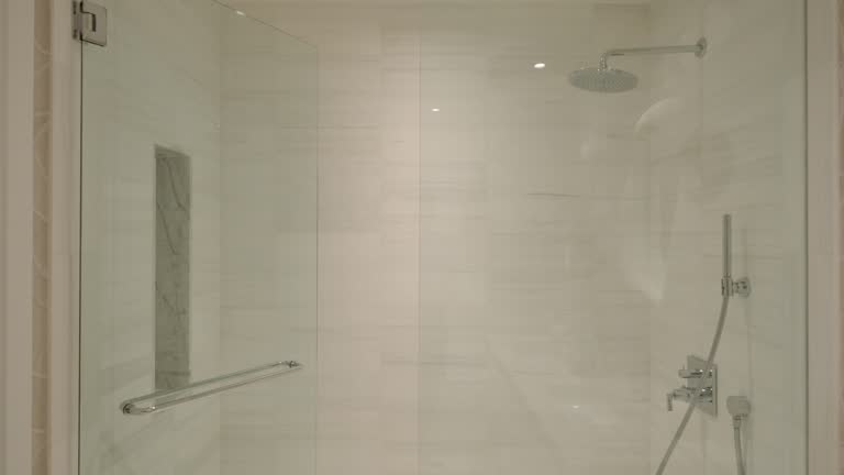 Glass walk in shower with rainfall head and handheld unit combines style and function. Soft neutral walls and built in lighting create clean minimalist atmosphere.