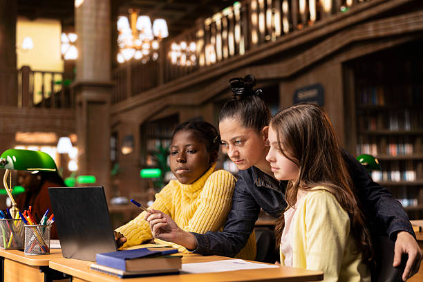 istock Caucasian tutor guiding two elementary school girls at a library desk 2213520842