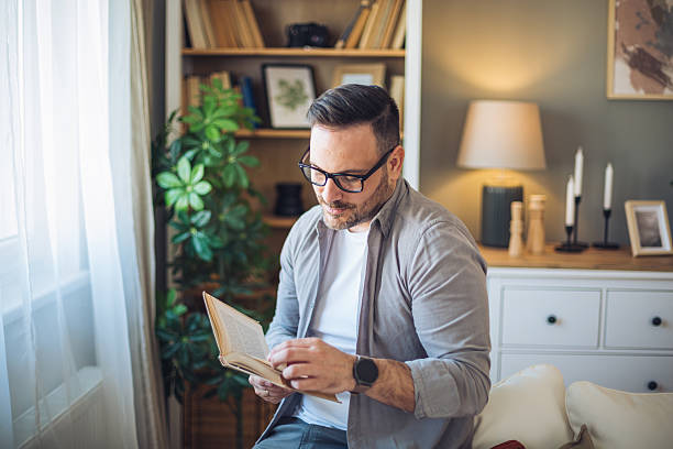 istock Mid adult man reading a book at home 2213528257