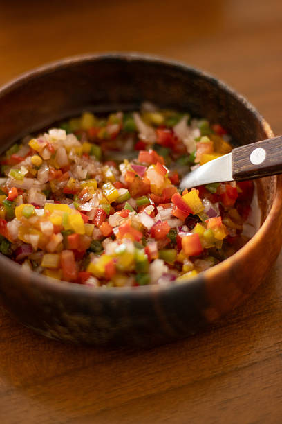 Sauce with yellow, green and red bell peppers and onions, used as topping for meats, sandwiches and other foods. Served on wooden bowl with spoon on the side