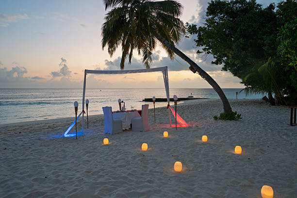 Romantic table setup on a tropical beach at sunset, with candles and soft lighting, creating a magical atmosphere