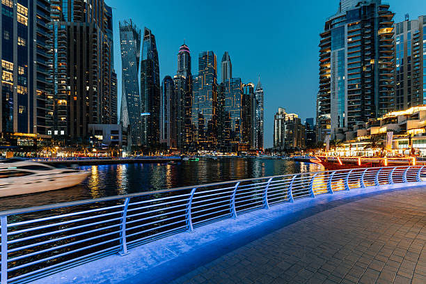 Modern Dubai Marina with illuminated skyscrapers and a moving yacht at blue hour in United Arab Emirates