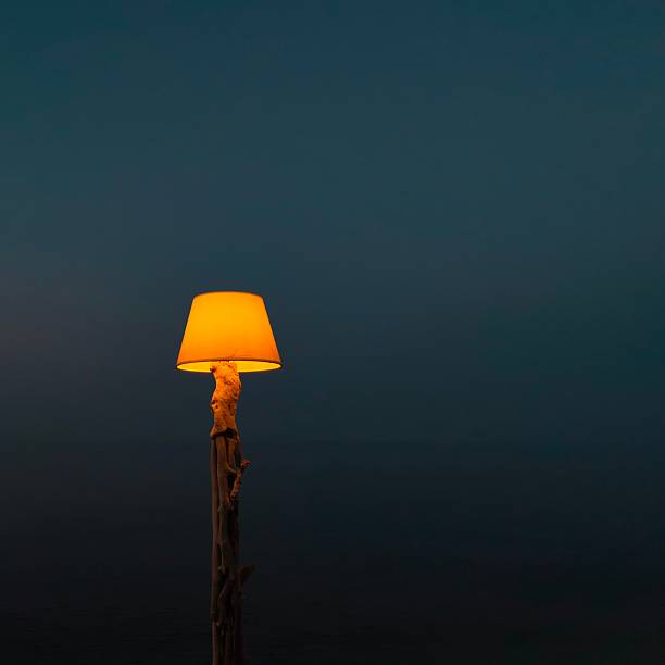 A glowing lamp with a yellow shade stands against a dark blue night sky, creating a warm and serene atmosphere.