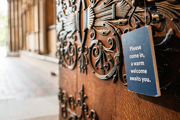 Shallow focus of a public visitor welcome sign seen hanging on an old, gothic door at the entrance to a famous English cathedral. stock photo