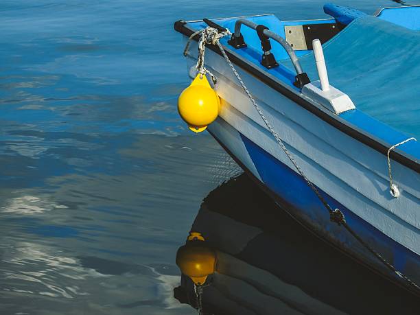 Close-up of a blue and white boat with a yellow buoy reflecting on calm water, creating a serene maritime scene.