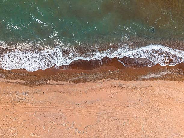 Aerial view of a sandy beach with gentle waves lapping on the shore, showcasing the serene coastal landscape.