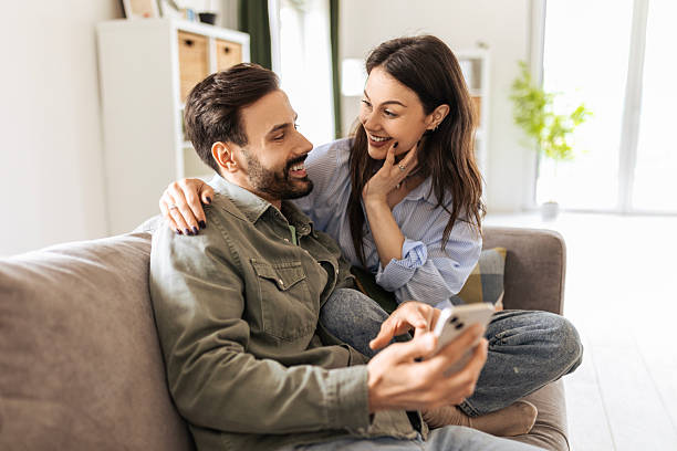 istock Young Couple Cuddling and Browsing Phone Together at Home 2213560011