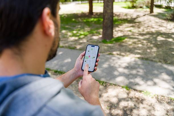 Young adult using a smartphone GPS app while walking in a park, focusing on navigation and location tracking. The scene emphasizes technology in daily life
