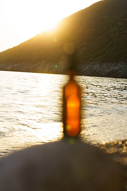 Vertical image selective focus brown mockup glass jar of serum with pipette on stone on background of sunset sea water and sun rays. Concept of beauty products, skin care, cosmetics