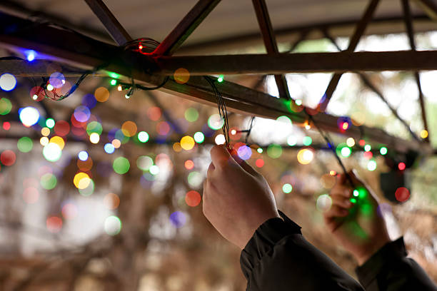 Man decorating house with Christmas lights outdoors, closeup. Space for text