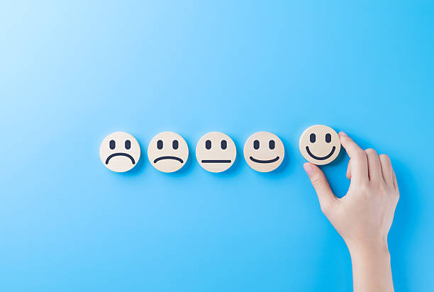 istock Customer Satisfaction Feedback and Rating Concept. Hand selecting smiling face icon from row of emoticons representing different satisfaction levels on blue background for feedback survey and review. 2213567685