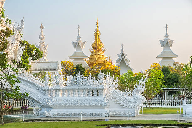 istock Golden and white Buddhist temple structures with intricate carvings surrounded by trees and greenery at sunset with, Chiang Rai, Thailand. Wat Rong Khun complex. Travel and touristic landmark 2213579079
