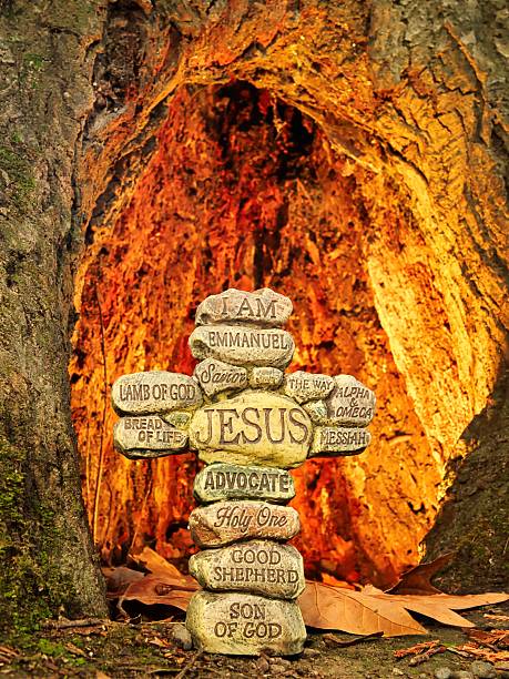 Stone cross with the names of Jesus Christ, with a warm lighted background of a inside tree.