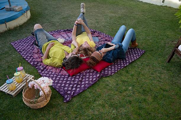 istock Three senior friends lying on a colorful mat in the backyard, enjoying a relaxing spring afternoon with drinks and a picnic basket 2213581784