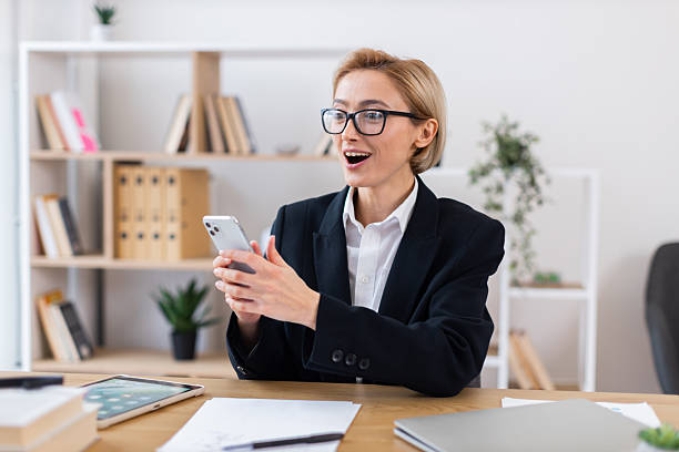 istock Surprised businesswoman using smartphone at office desk during workday 2213583932