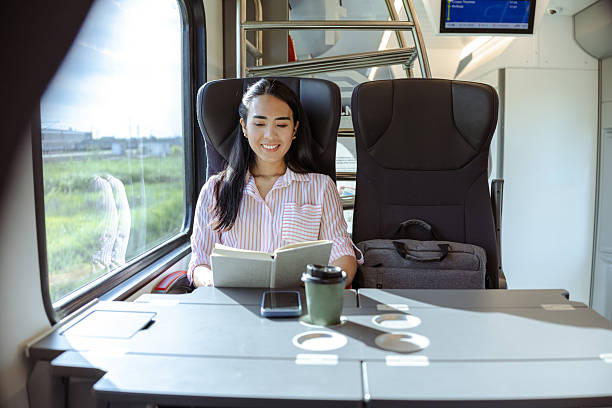 istock Young woman reading a book while traveling comfortably on a train 2213592788