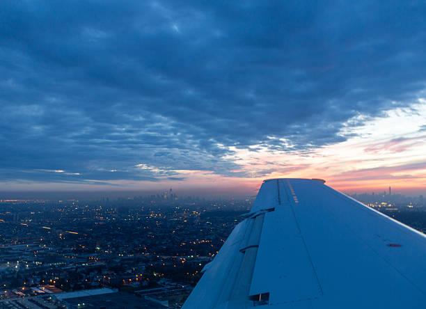 Sunset and clouds over an airplane wing as it flies over the lights of a city at a lower altitude on a trip up the eastern seaboard