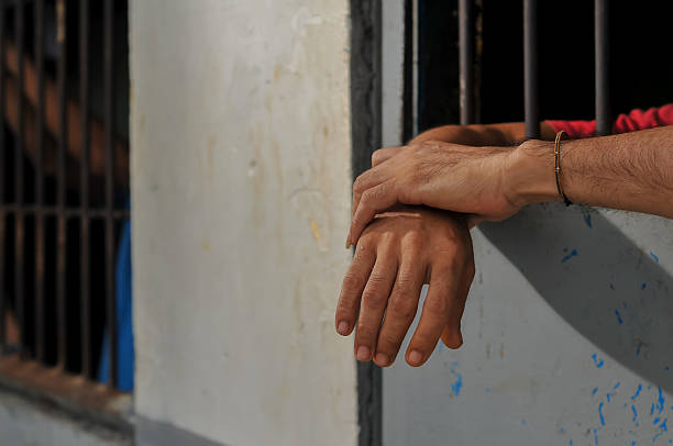 istock hands of a prisoner behind prison bars on black background 2213612604