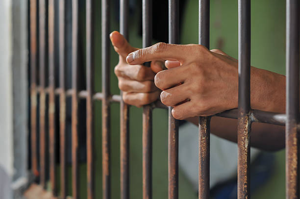 istock hands of a prisoner behind prison bars on black background 2213612701