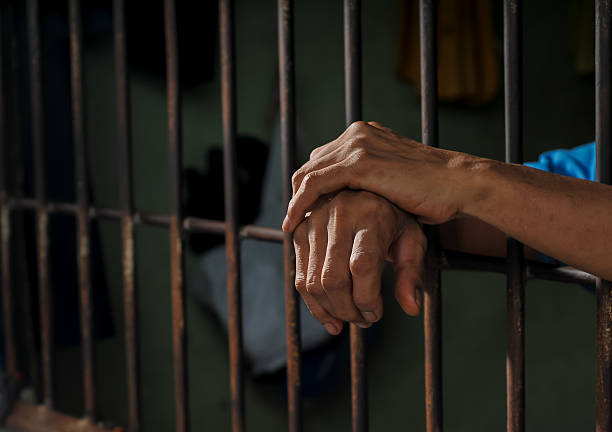 istock hands of a prisoner behind prison bars on black background 2213612706