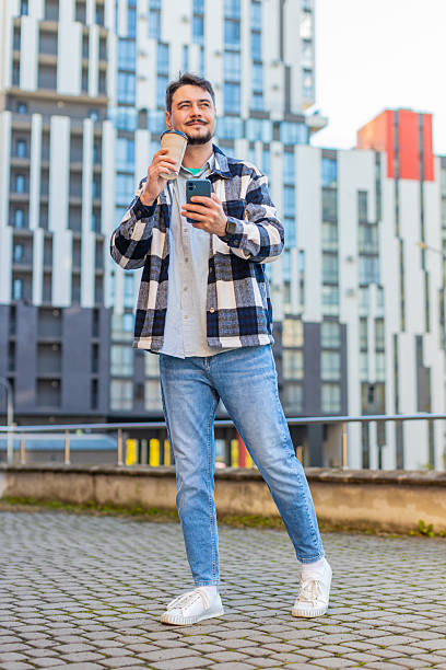 istock Happy man using smartphone while enjoying morning to-go coffee hot drink against modern building 2213615123