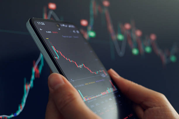 istock A hand holds a smartphone displaying a declining stock market chart against a blurred background of similar data. 2213627063