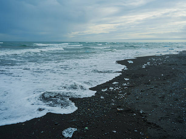 Scenic landscape of icebergs on black sand at Diamond Beach, Iceland, during sunrise. The glowing ice contrasts against the volcanic shore, capturing the surreal beauty of nature in transition.