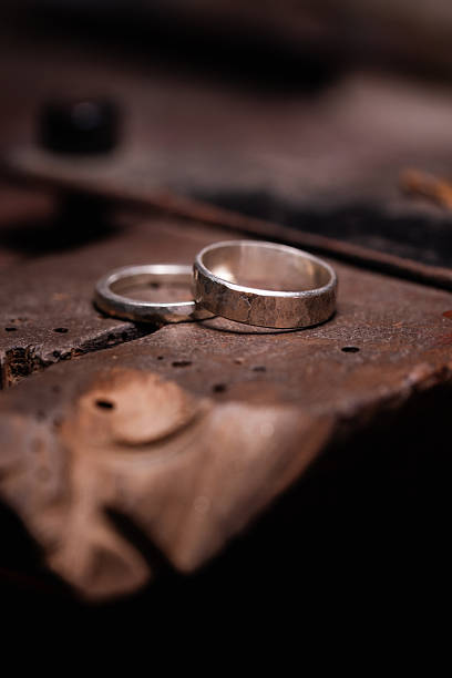 istock Two Handcrafted Silver Wedding Rings Resting on a Worn Wooden Bench Pin 2213654885