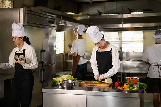 istock Busy cooking class in session with multiple students in uniforms preparing fresh ingredients 2213655007