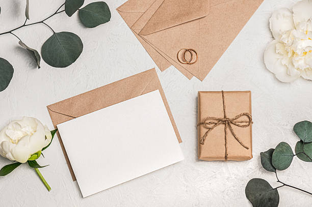 istock Wedding invitation or greeting card mockup with craft envelope, gift box, white peony flowers and eucalyptus sprigs and wedding rings on light background. 2213658678