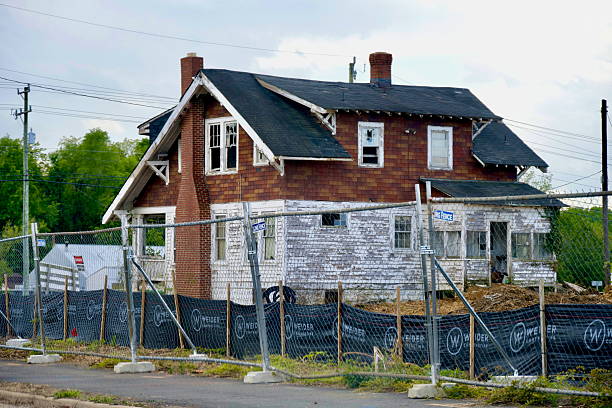 Fairfax, Virginia, USA - May 2, 2025: A dilapidated house with broken windows and peeling paint is fenced off at a new development construction site in Fairfax County.
