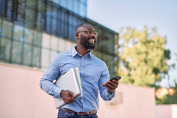 istock Smiling businessman walking and using smartphone near office building 2213659172