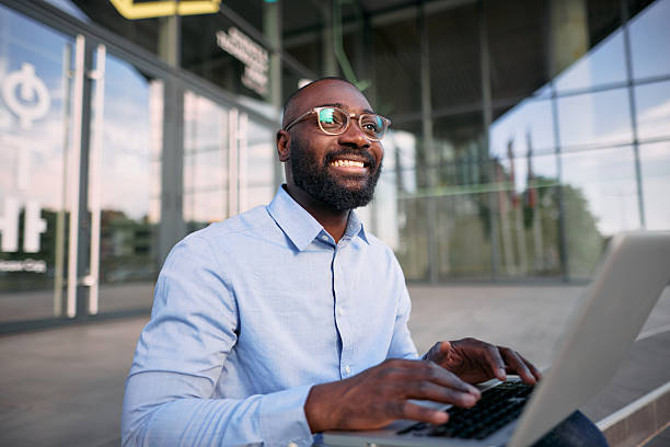 istock Smiling businessman working with laptop outside office building 2213659328